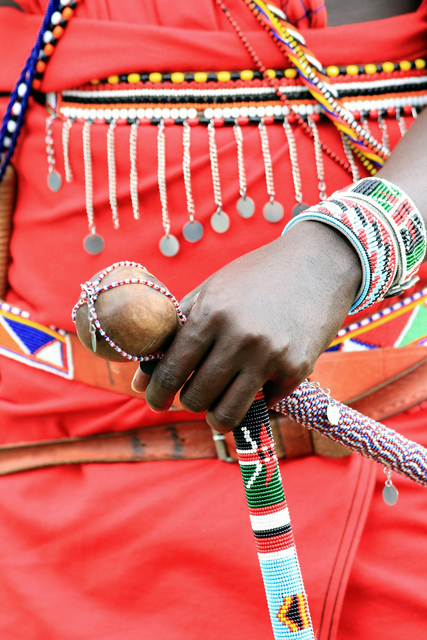 A hand wearing beaded wristbands in red, white, green and black against a red shuka, Kenya
